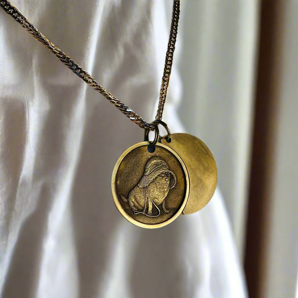 Two shiny stainless steel bar pendant necklaces in gold and silver finishes, with custom paw print engravings on each, placed on linen fabric with lavender and twine for decoration.