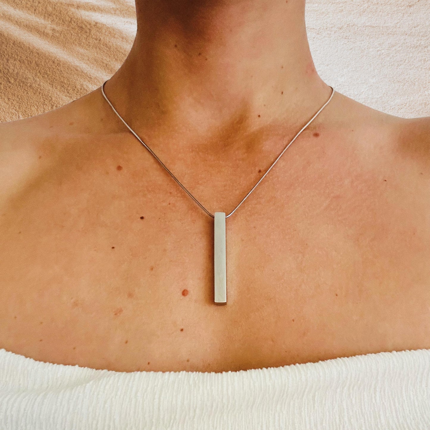 Necklace with a rectangular pendant worn by a person against a neutral background