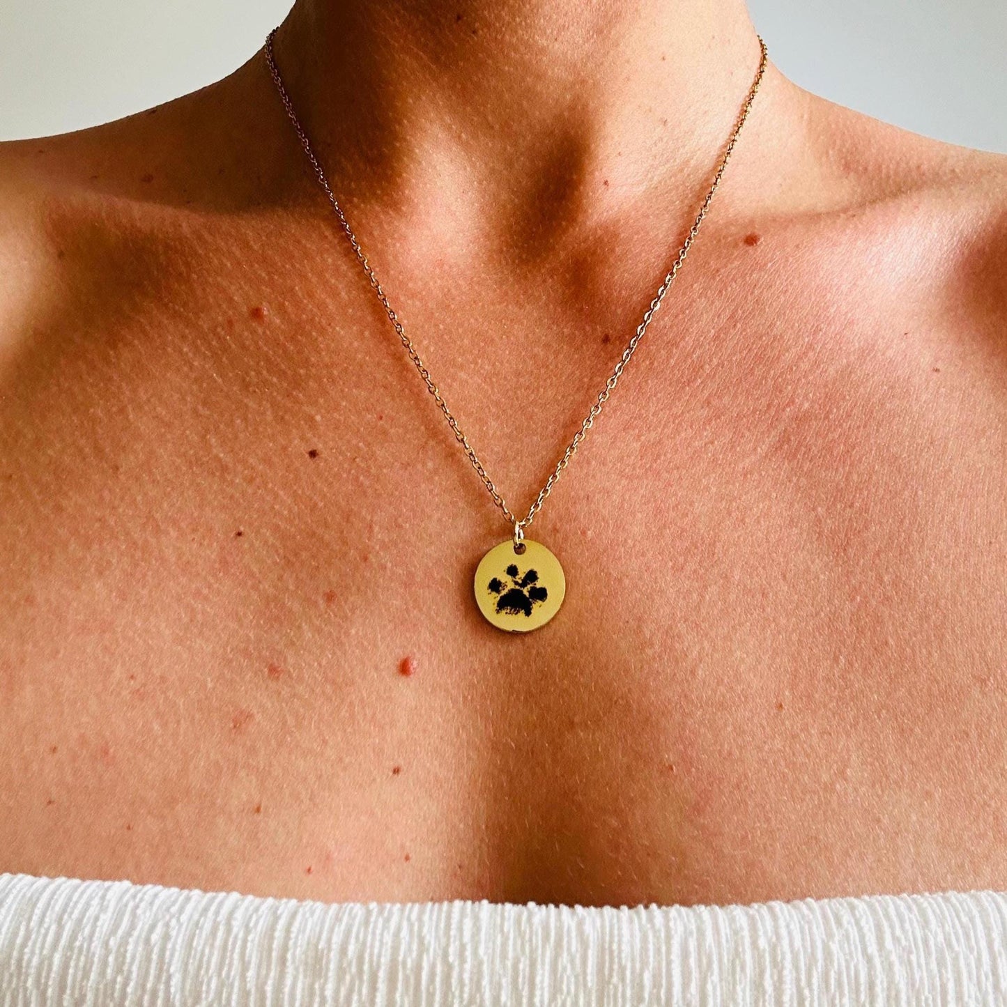 Gold necklace with a paw print pendant on a person's neck