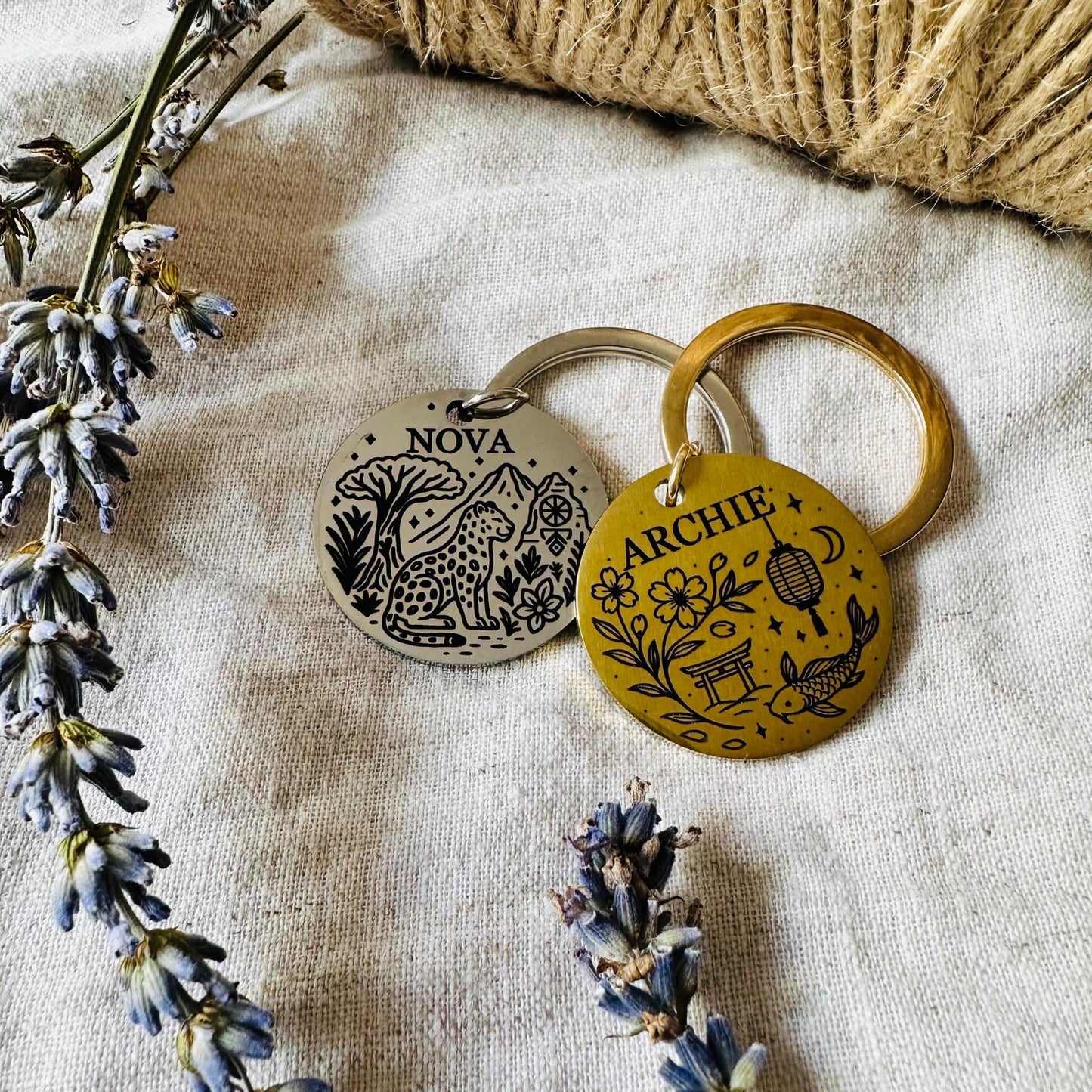Two dog tag with engraved names on a textured fabric background with lavender flowers.