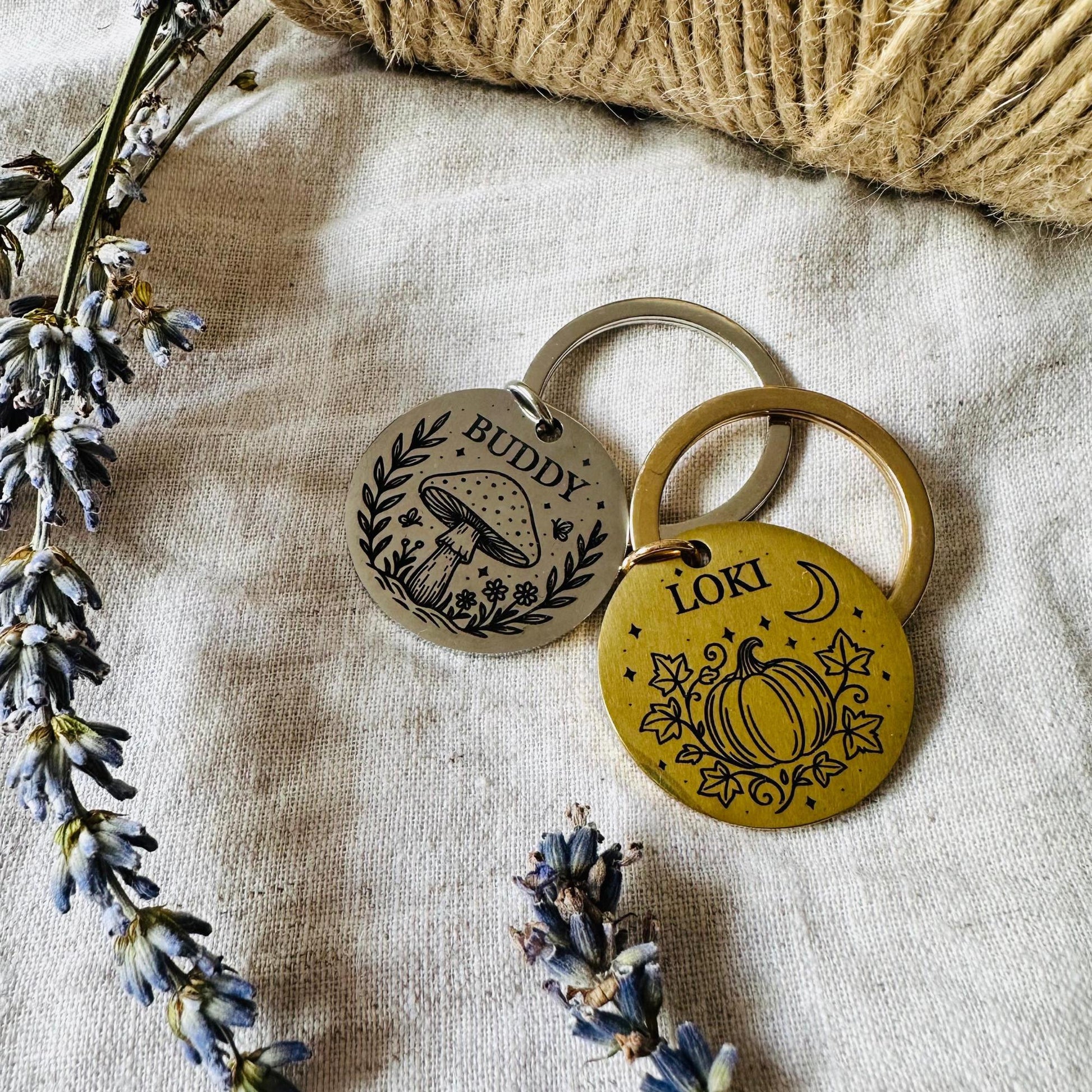 Two dog tag with engraved designs on a textured fabric background with lavender flowers.