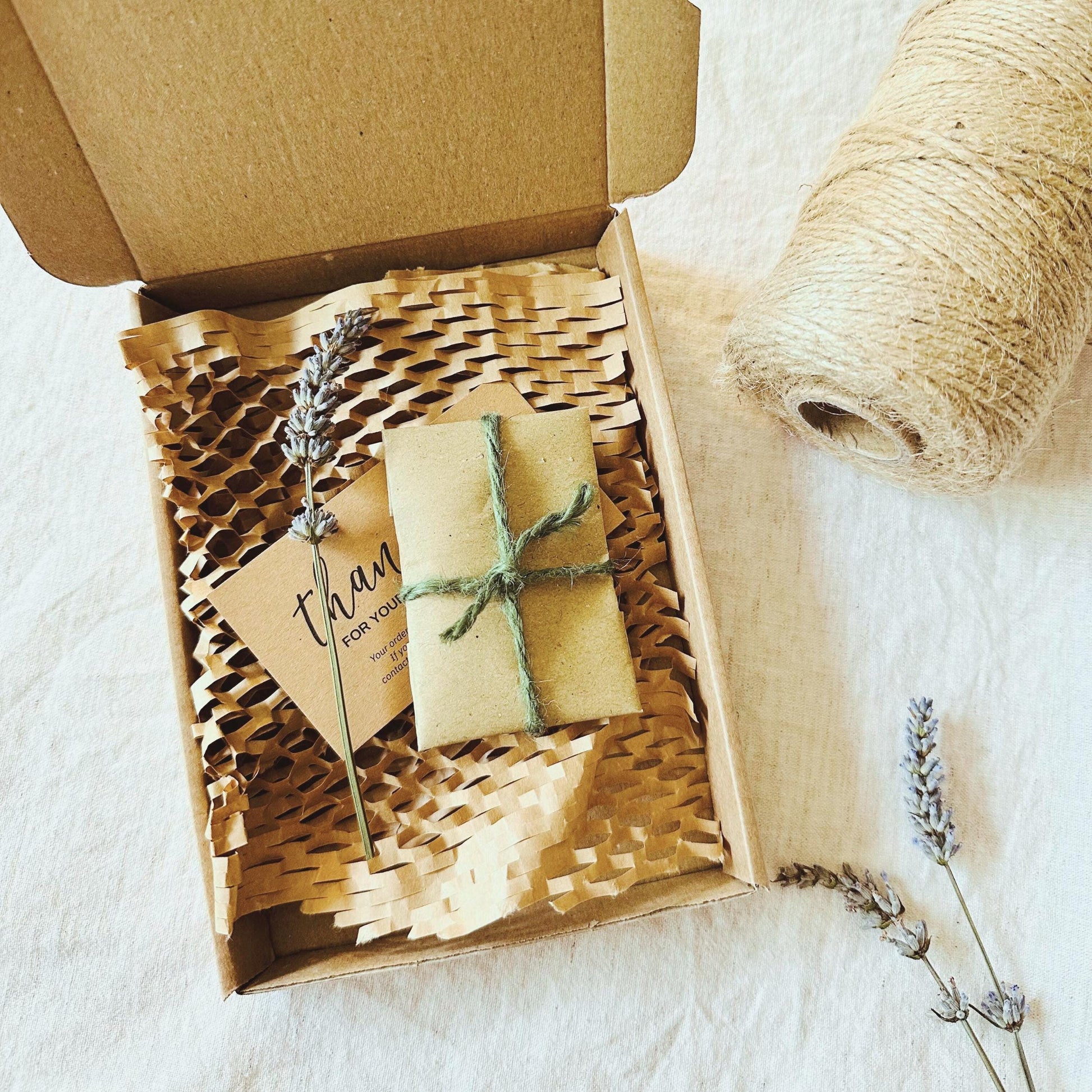 Gift box with a small wrapped package and a card inside, surrounded by lavender and twine on a light background.