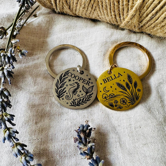 Two dog tag with engraved designs and names on a textured fabric background.