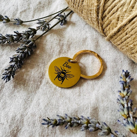 Gold Dog tag with bee design on a textured surface with lavender and twine.