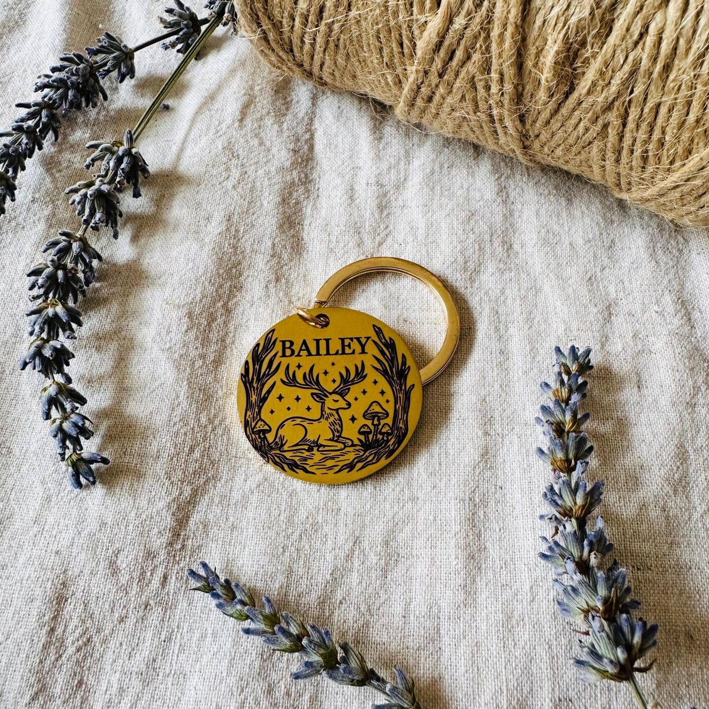 Gold dog tag with 'BAILEY' engraving on a textured surface with lavender and yarn.