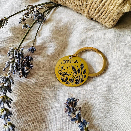 Gold Dog tag with 'Bella' engraved, surrounded by dried lavender on a textured fabric background