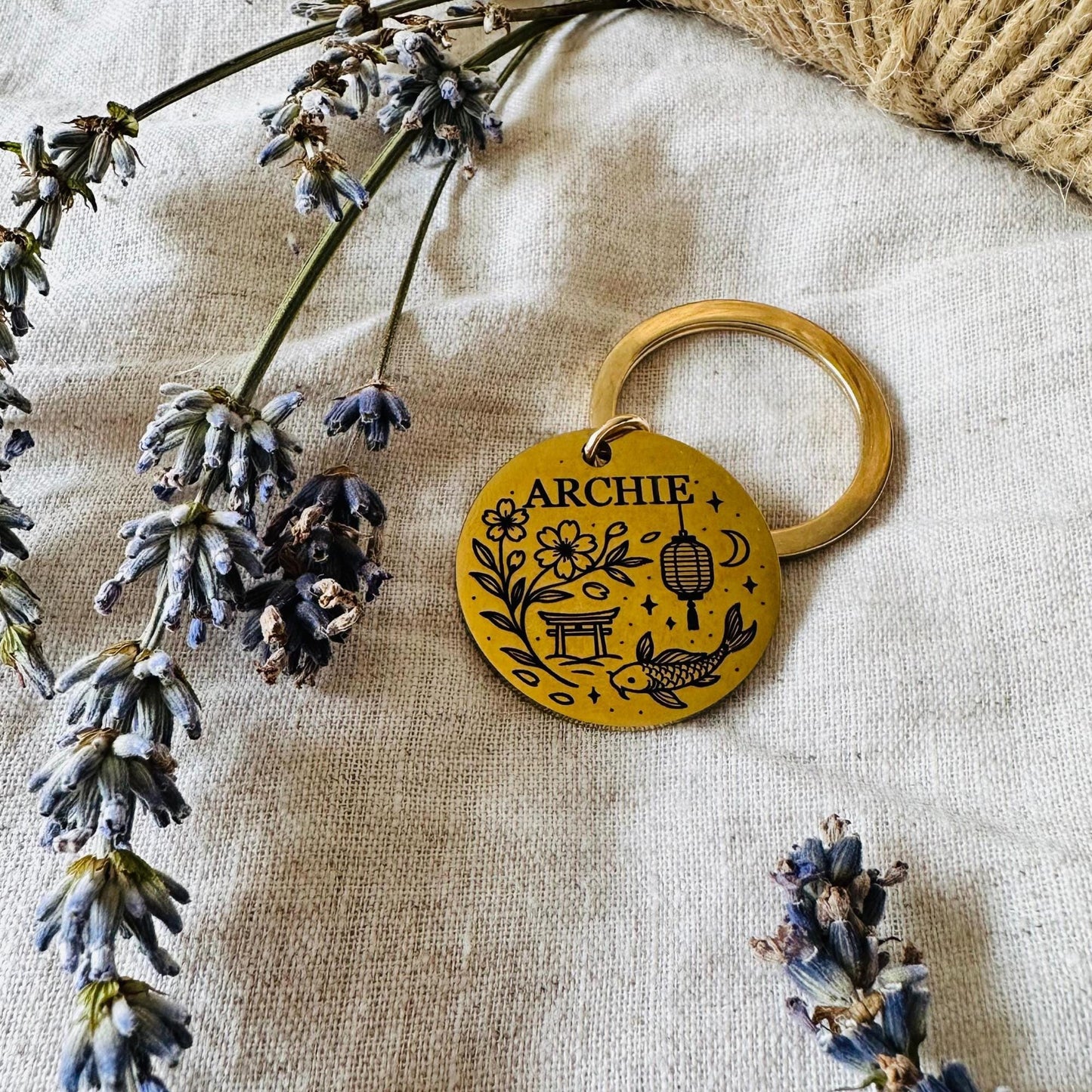 Dog tag with 'ARCHIE' engraving on a textured fabric background with lavender flowers.