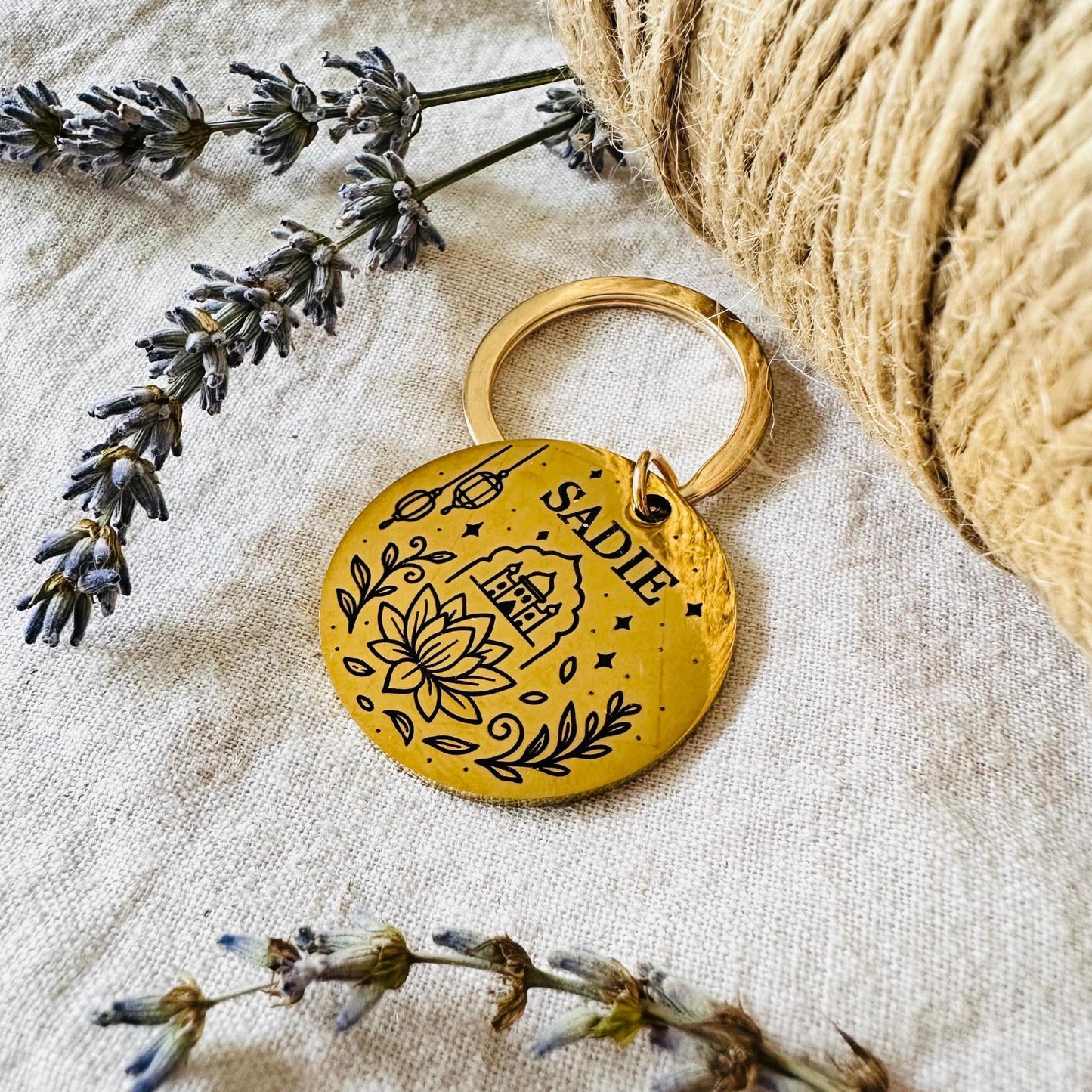 Gold keychain with 'SADIE' engraved on a textured surface with lavender and twine.