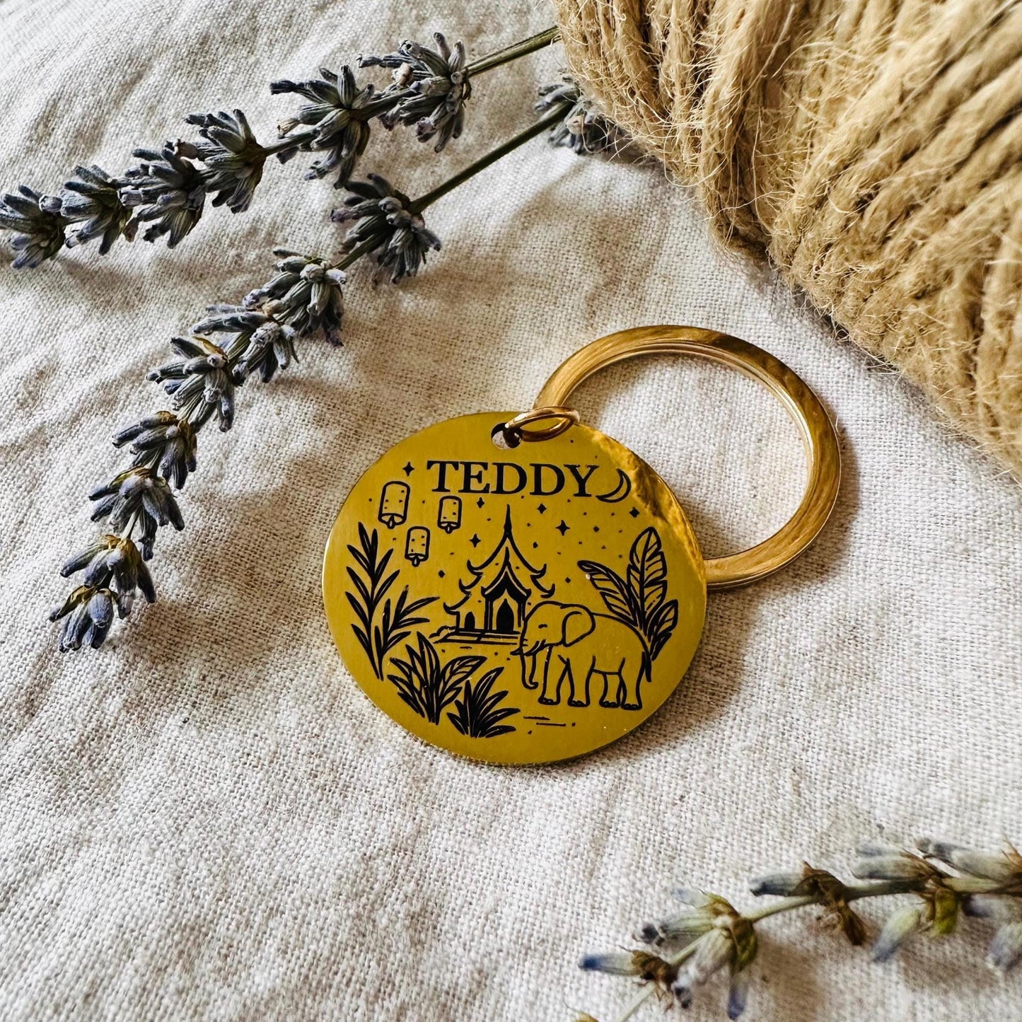 Gold dog tag with 'TEDDY' branding on a textured surface with lavender and twine.
