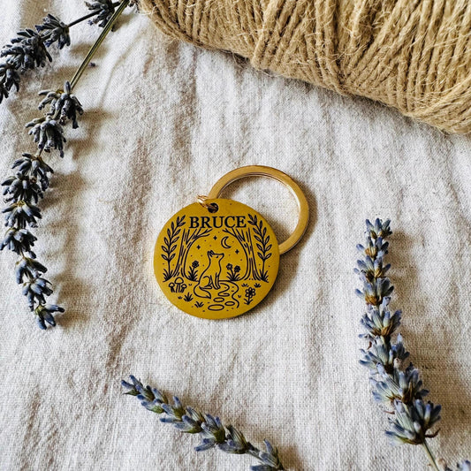 Golden Dog tag with 'BRUCE' engraving on a textured fabric background with lavender.