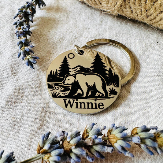 Gold keychain with bear design and 'Winnie' engraving on a textured fabric background with lavender.