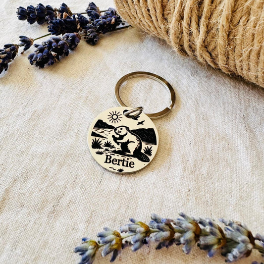 Pet id tag with beaver design and 'Bertie' engraving on a textured surface with lavender flowers.