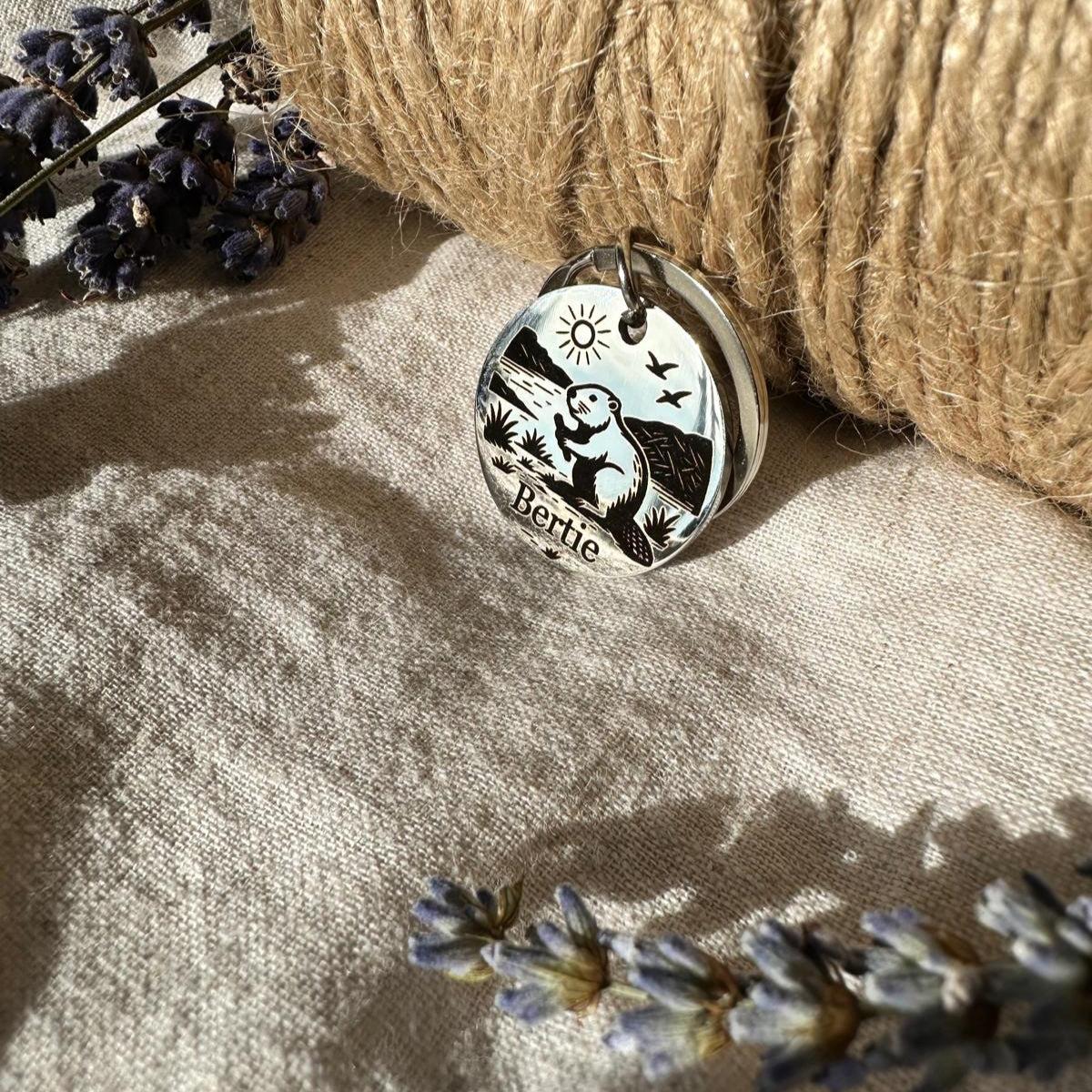 Silver pendant with beaver design on a textured surface with twine and lavender flowers.
