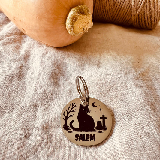 Dog tag with a cat silhouette and 'Salem' text on a rustic fabric background and a pumpkin.