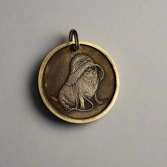 Bronze pendant with a engraved design on a grey surface