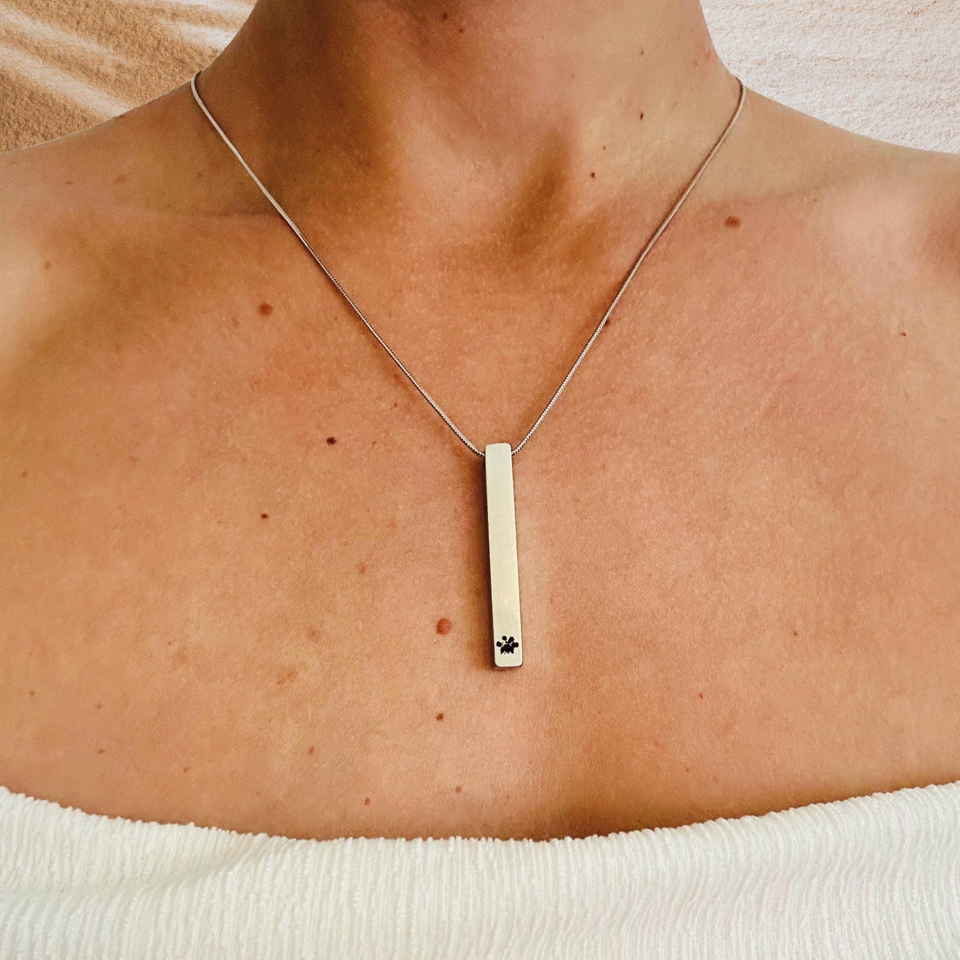 Necklace with a bar pendant on a person's neck against a neutral background