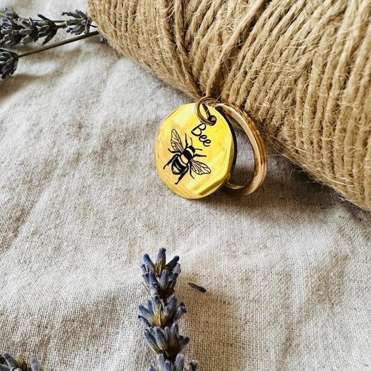 Gold charm with bee design on a textured fabric background with lavender flowers