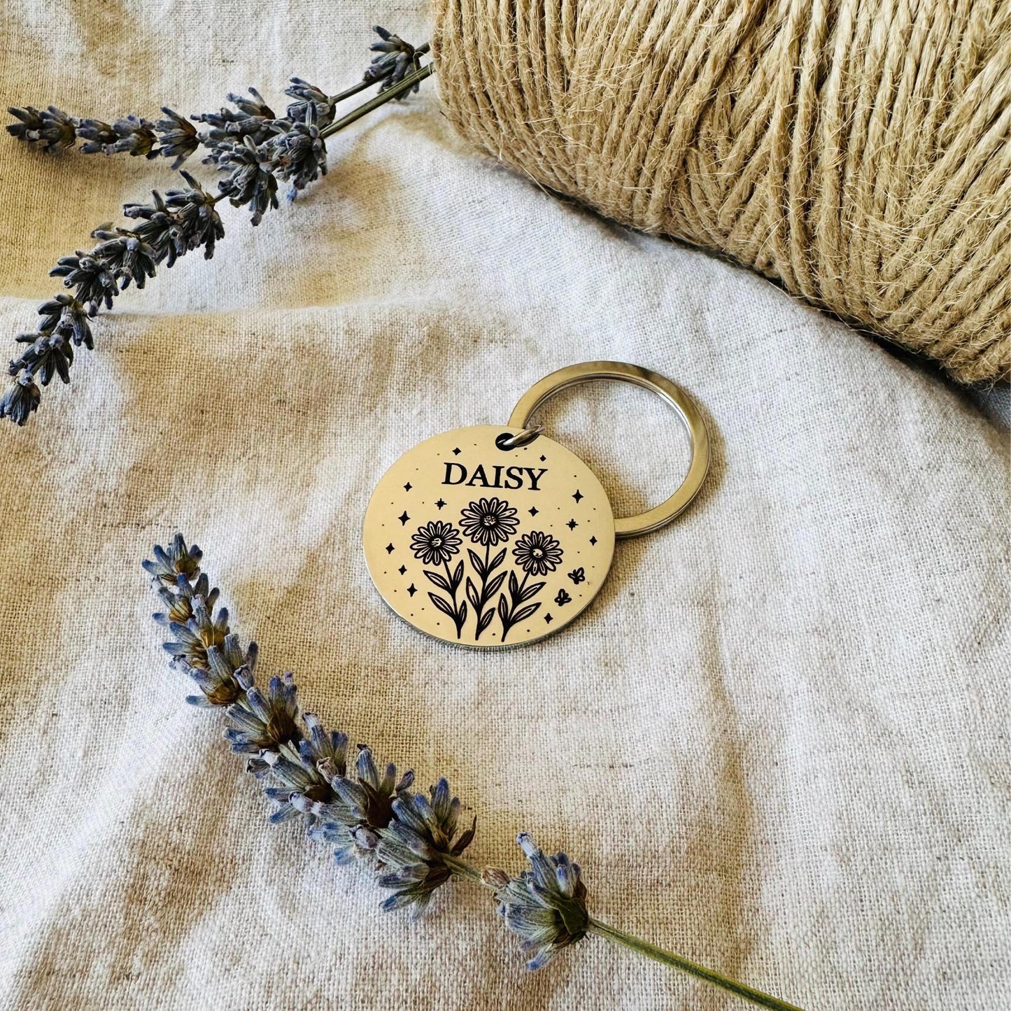 Pet ID tag with 'DAISY' engraving on a textured fabric background with daisy flowers.