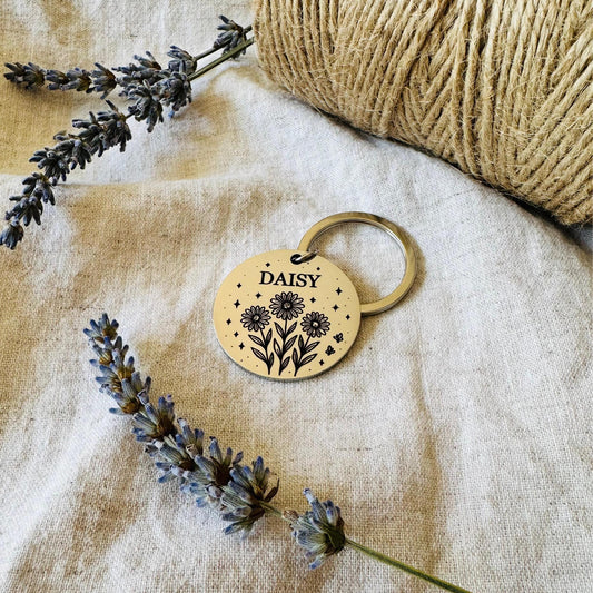 Pet ID tag with 'DAISY' engraving on a textured fabric background with daisy flowers.