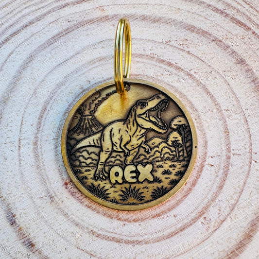 Brass antique style deep engraved pendant with dinosaur design and 'Rex' text on a wooden surface