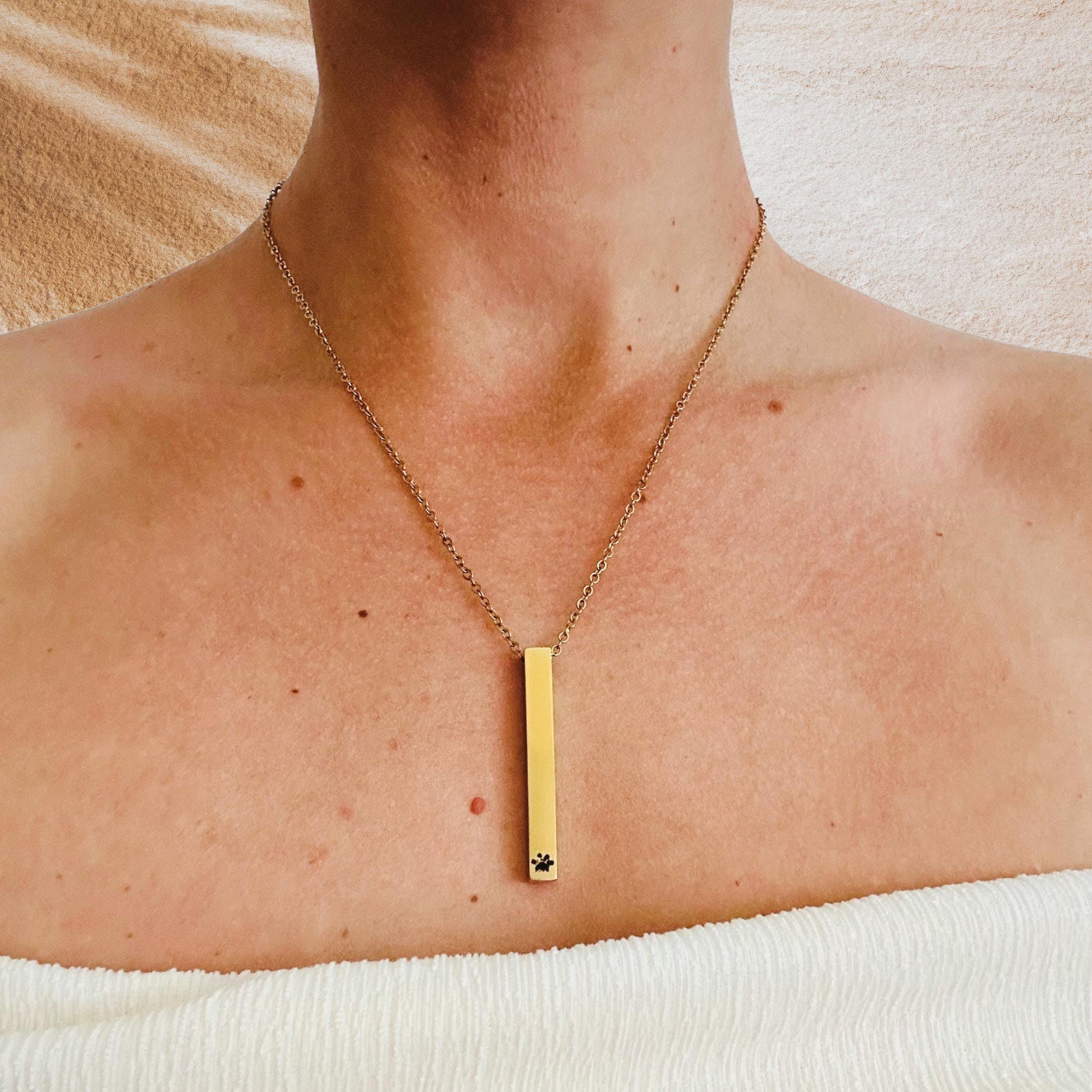 Gold necklace with a vertical pendant on a person's neck against a neutral background