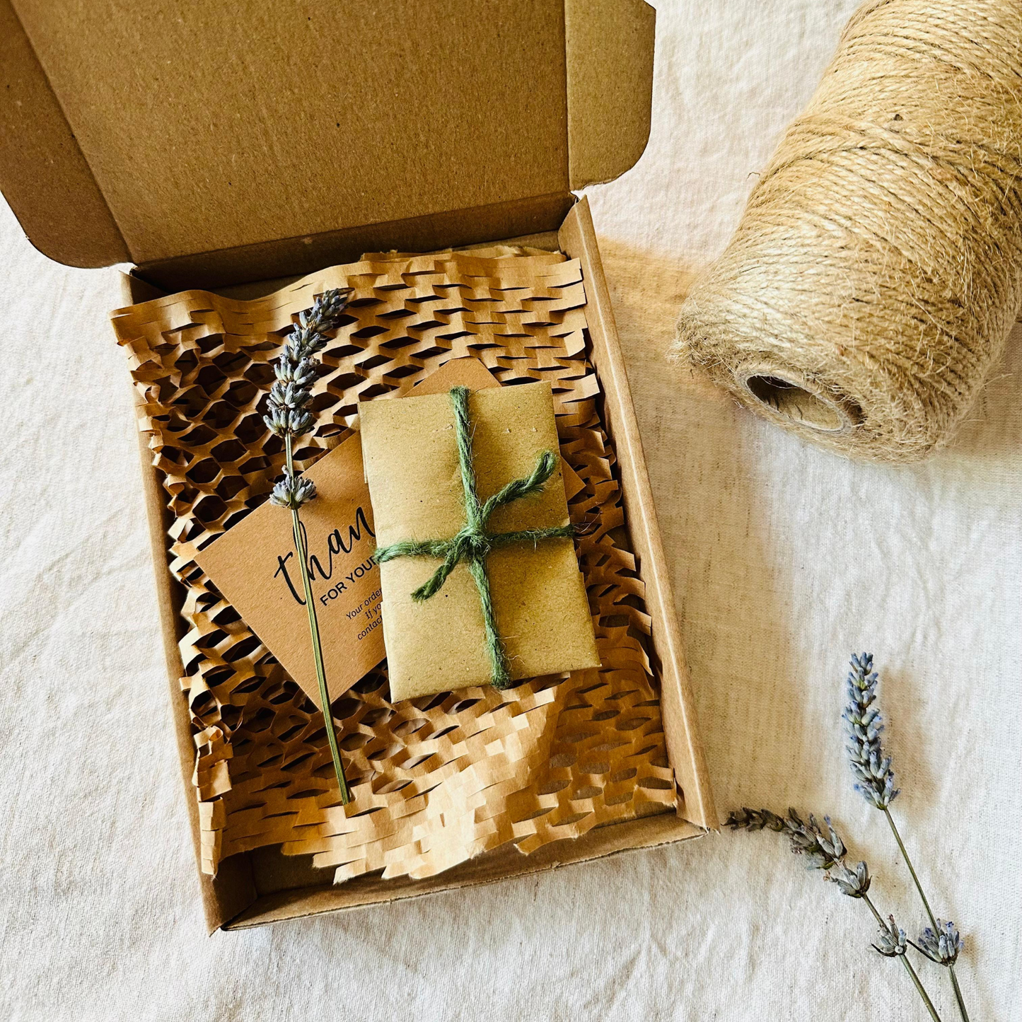 Gift box with a wrapped item, card, and lavender sprigs on a textured surface.