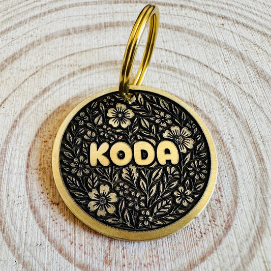 Gold and black floral deep engraved pet ID tag on a wooden background. 