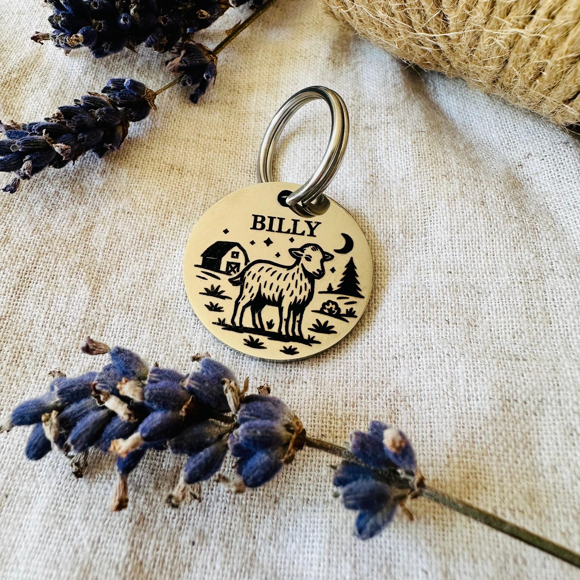 Gold keychain with engraved design of a sheep and text 'BILLY' on a textured surface with lavender flowers.