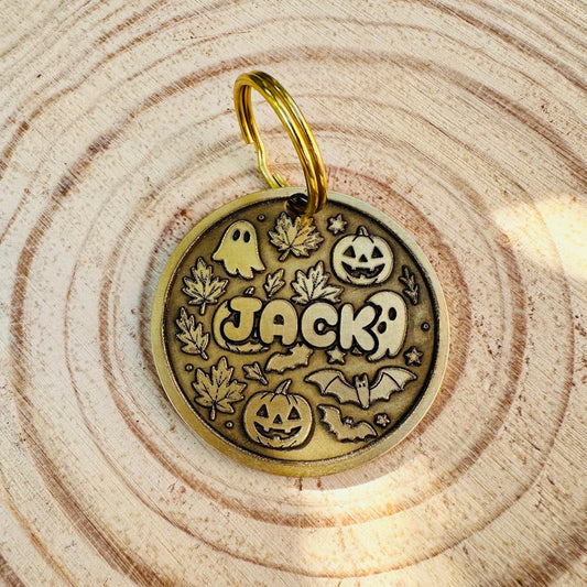 Brass halloween design pet id tag with ghosts, bats, pumpkins and leaves, laying on a wooden slab
