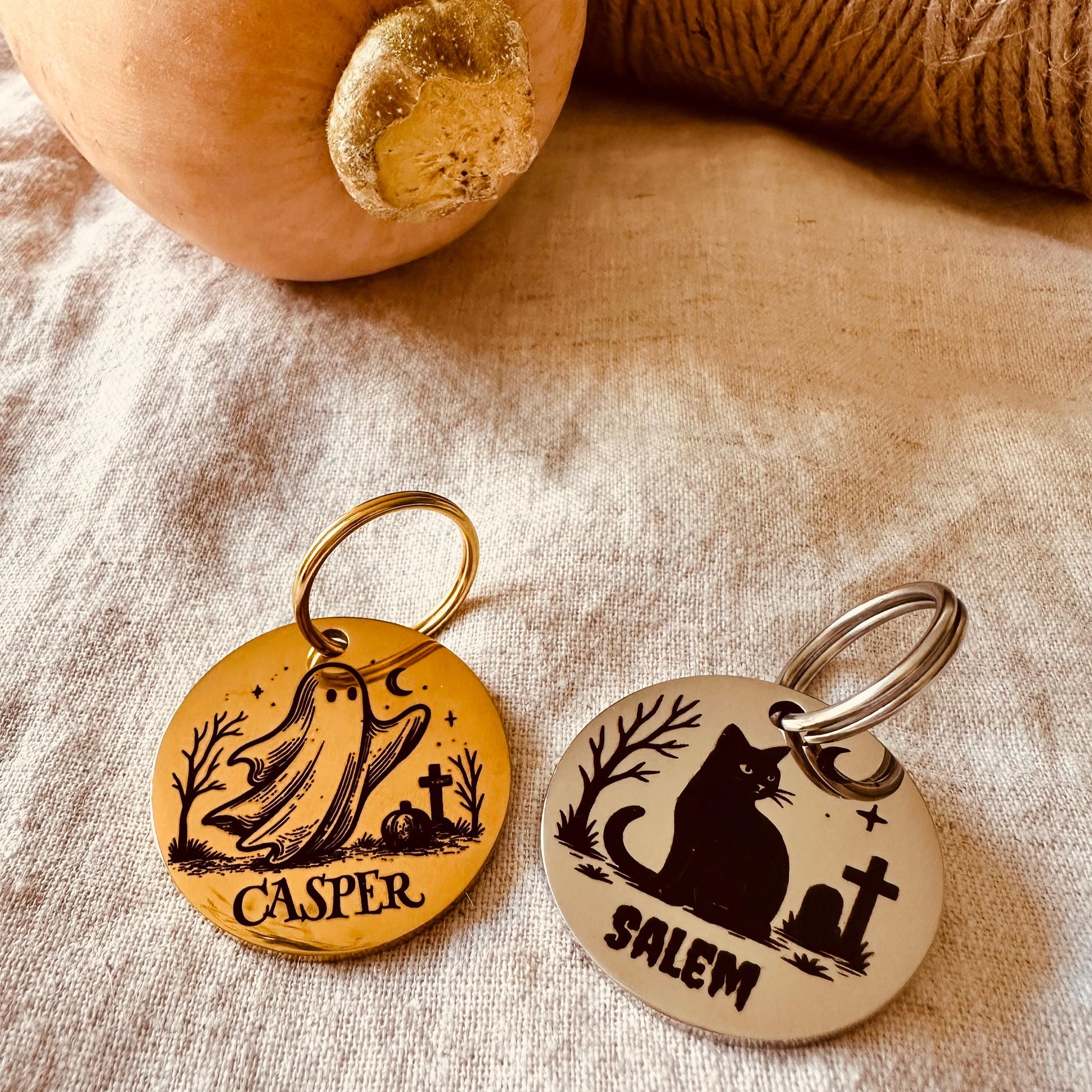 Two Halloween-themed pet tags with 'Casper' and 'Salem' on a textured fabric background with pumpkin and twine.