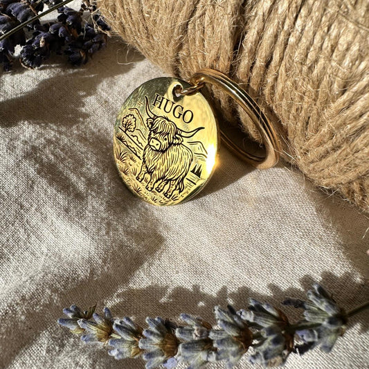 Gold pendant with 'HUGO' engraved, placed on a textured surface with lavender flowers.