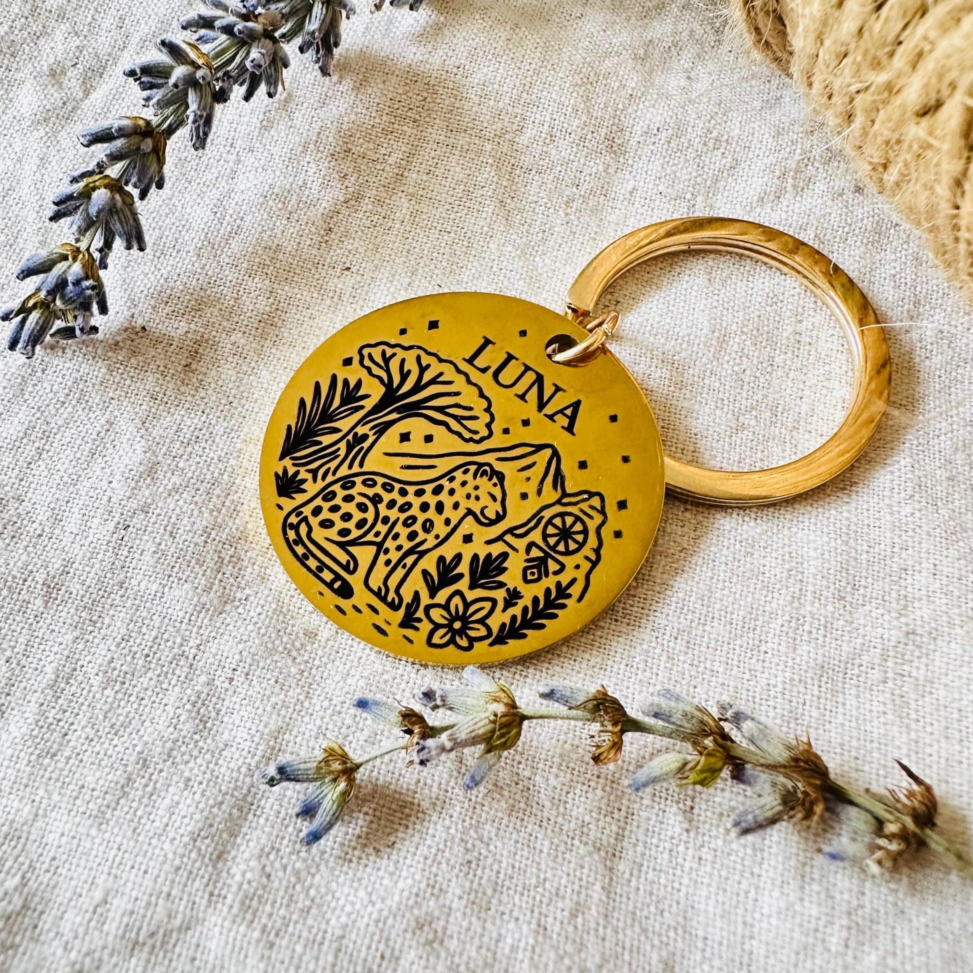 Yellow keychain with leopard design and 'LUNA' text on a textured fabric background with lavender and dried flowers.