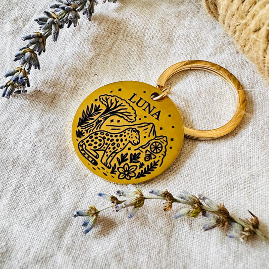 Yellow keychain with leopard design and 'LUNA' text on a textured fabric background with lavender and dried flowers.