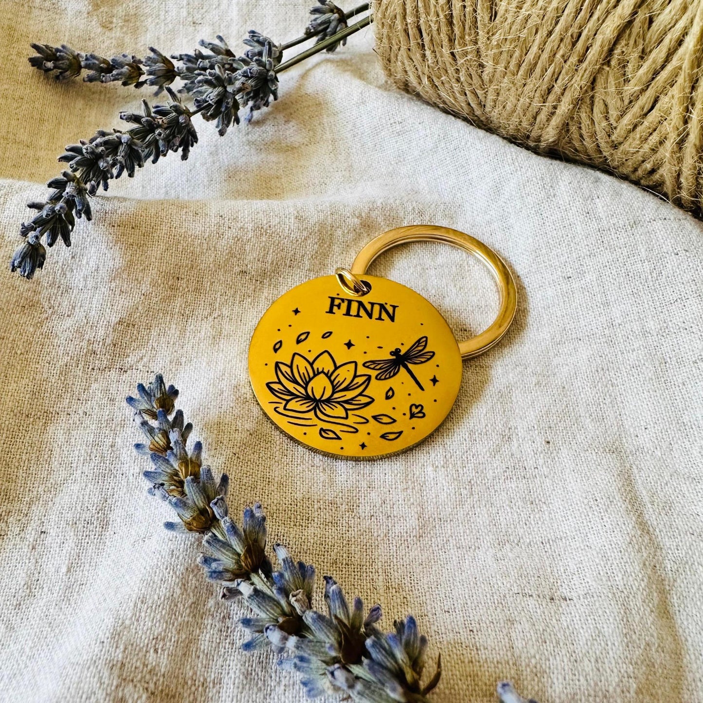 Gold dog tag with 'FINN' engraved, surrounded by lavender and twine on a textured fabric background
