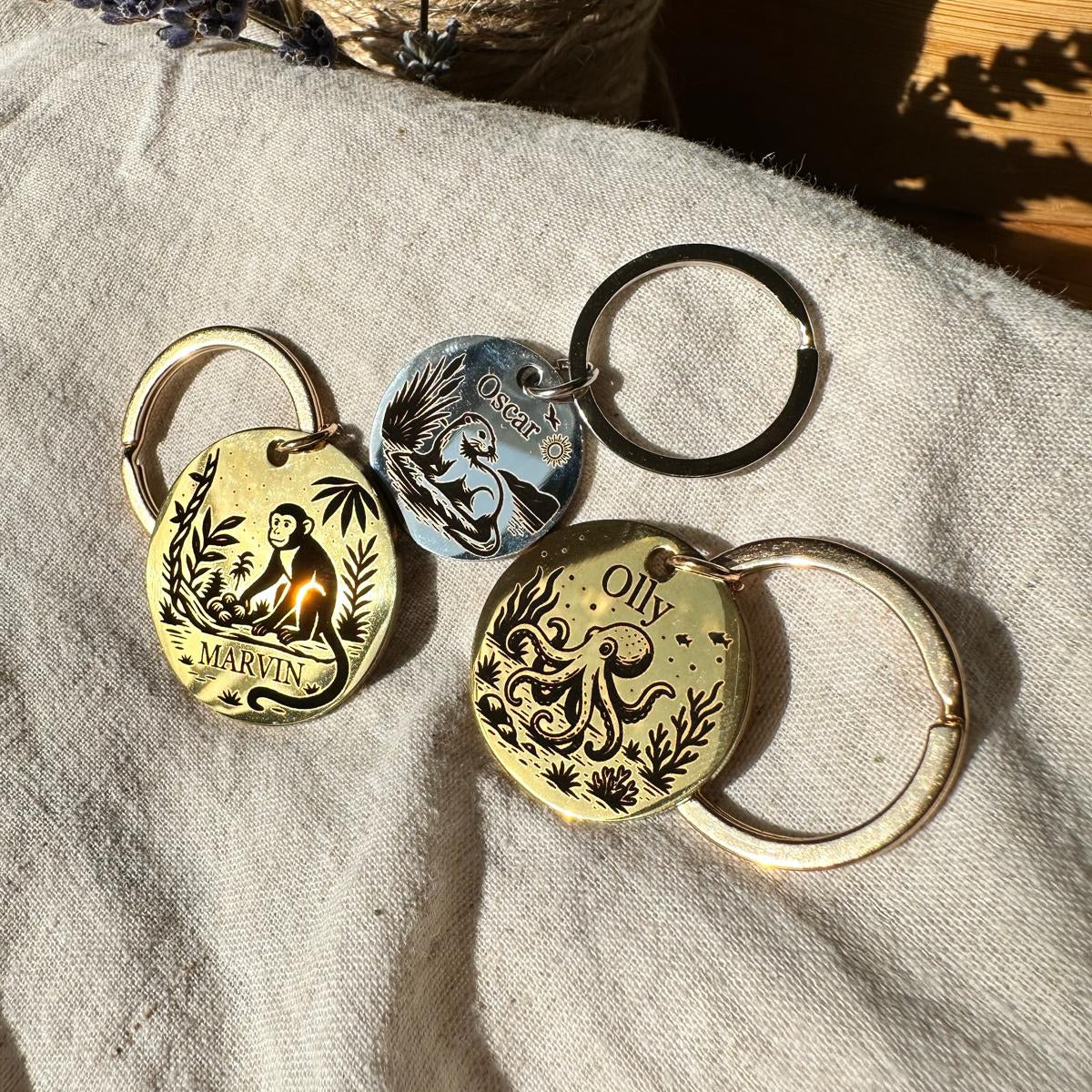 Three pet id tags with engraved designs including monkey, octopus and beaver on a textured fabric surface.