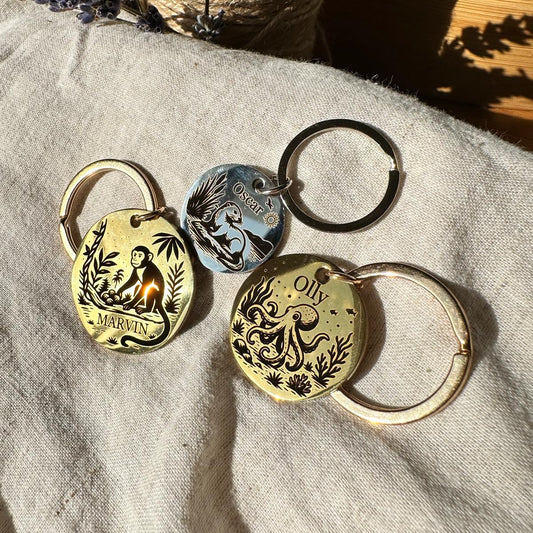 Three pet id tags with engraved designs including monkey, octopus and beaver on a textured fabric surface.