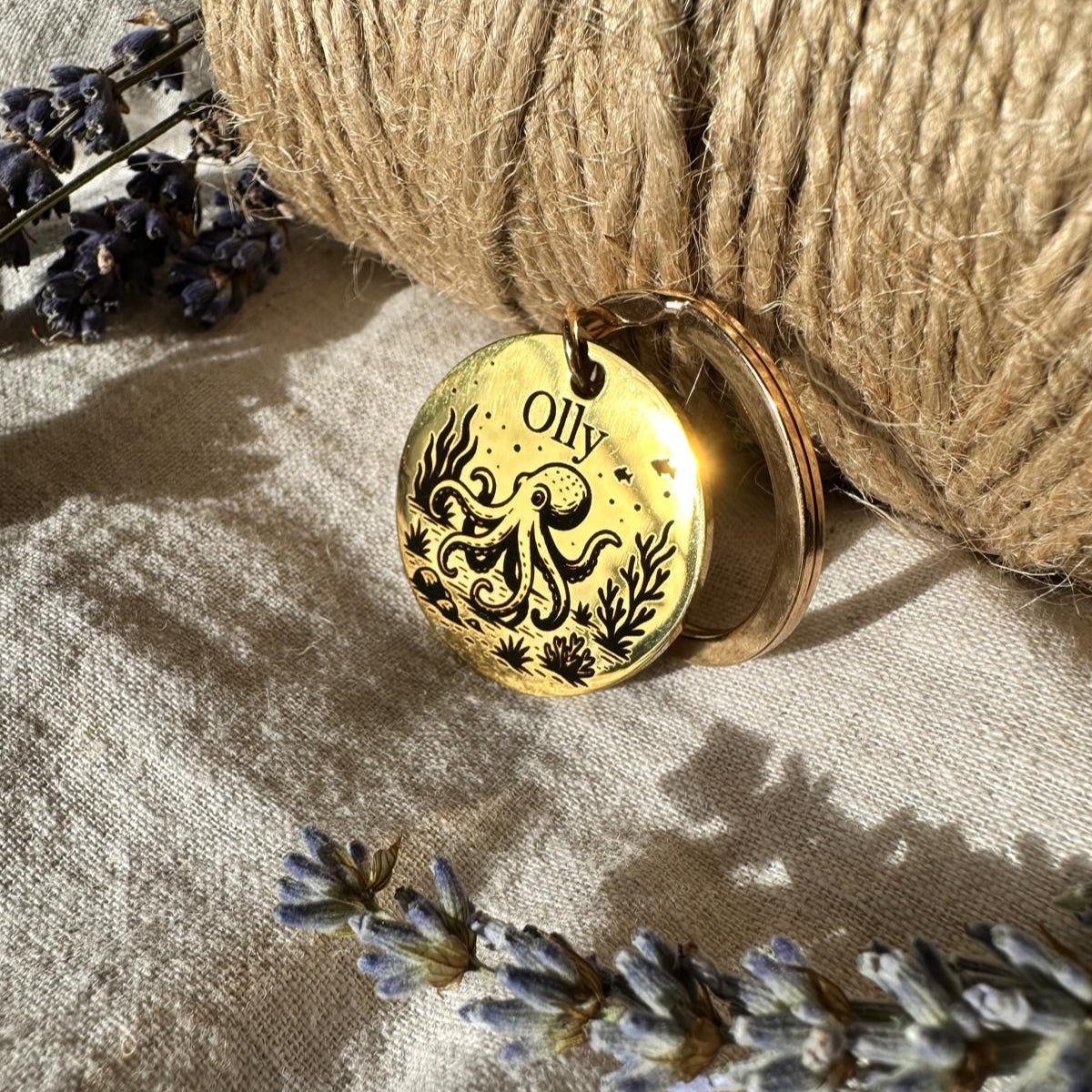 Gold pendant with 'Olly' engraving placed on a textured surface with lavender flowers