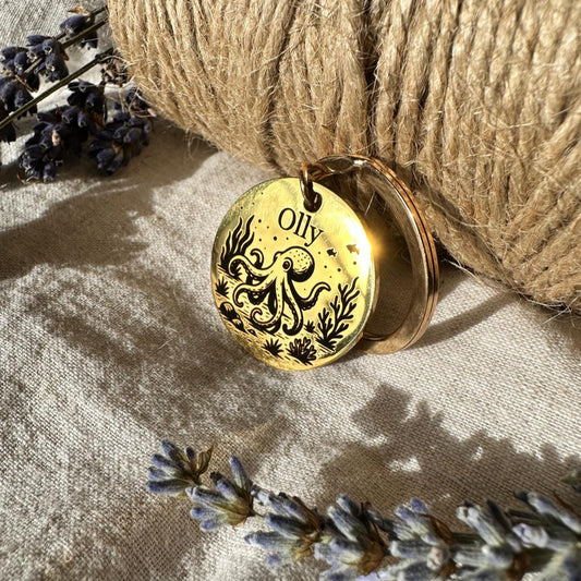 Gold pendant with 'Olly' engraving placed on a textured surface with lavender flowers