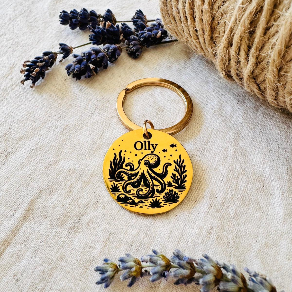 Pet id tag with underwater design  featuring an octopus and 'Ollly' written on it, placed on top of  a textured surface with lavender and twine.