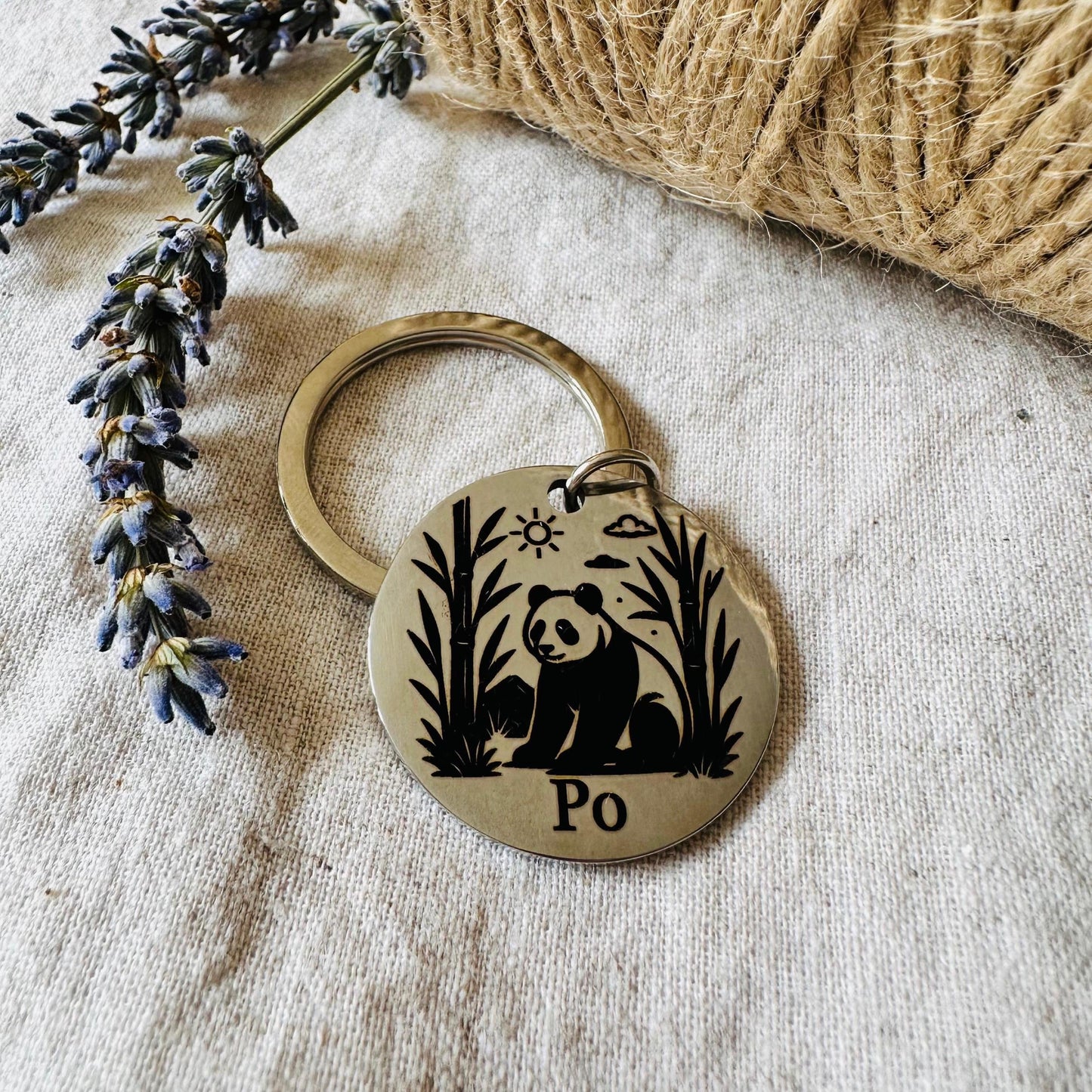 Dog tag with panda design and 'Po' text on a textured surface with lavender and twine.