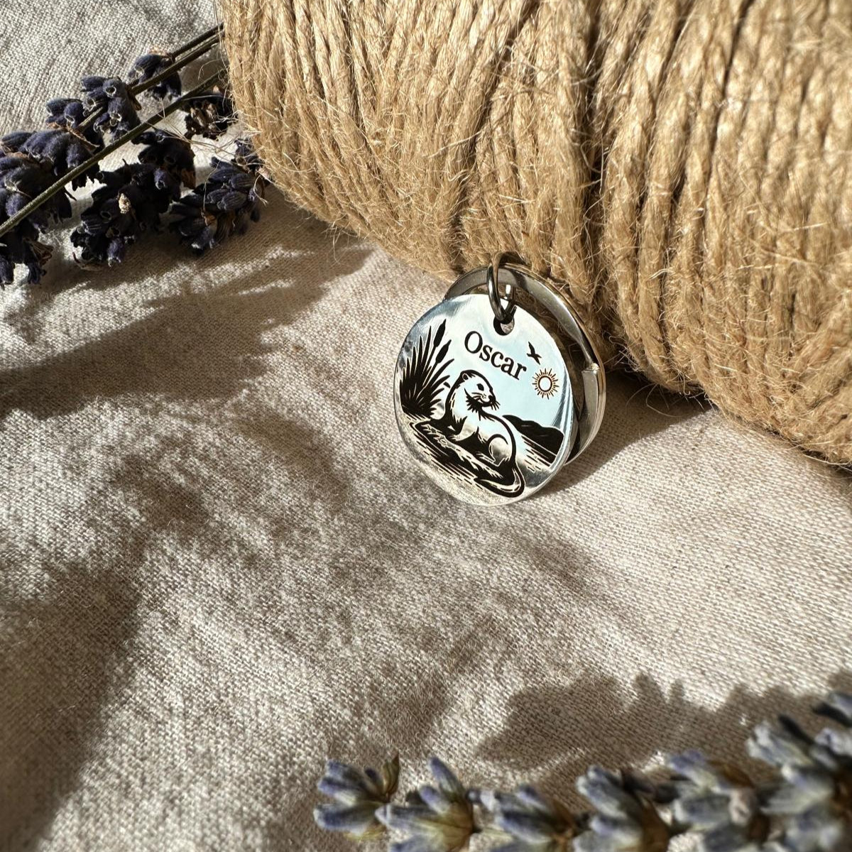 Silver pendant with engraved design on a textured surface with twine and lavender flowers.