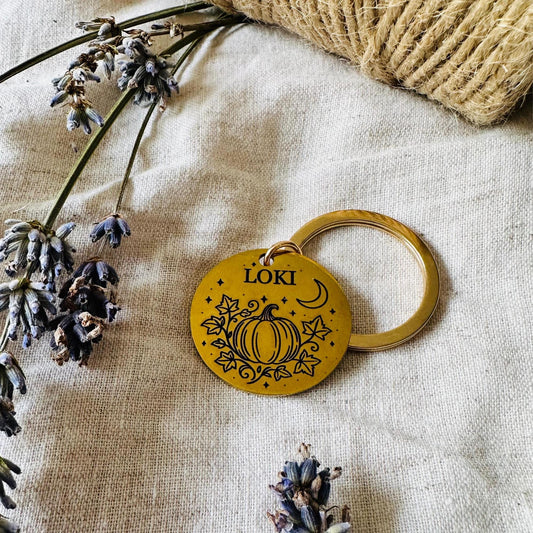 Gold dog tag with 'LOKI' engraving on a textured fabric background with dried lavender and twine.