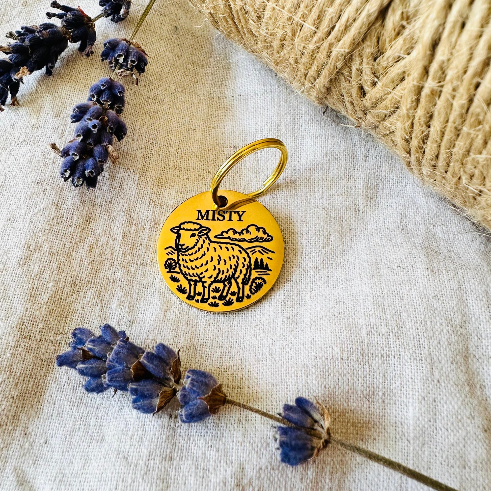 Gold finish stainless steel pet id tag with sheep design on a textured fabric background with lavender flowers