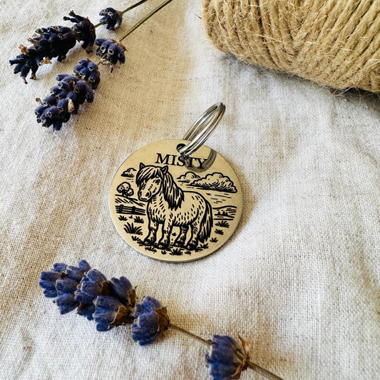 Round stainless steel pet id tag in silver with horse design on a textured fabric background with lavender flowers and twine.