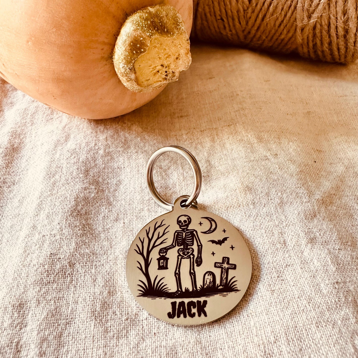 Stainless steel pendant with skeleton design and 'Jack' text on a textured fabric background.
