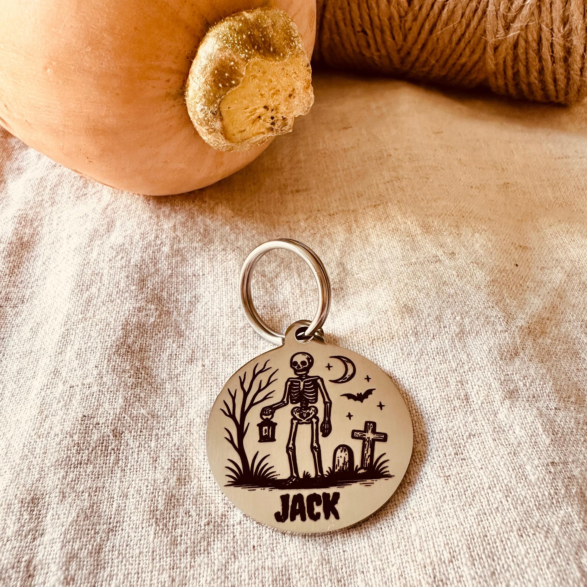 Stainless steel pendant with skeleton design and 'Jack' text on a textured fabric background.