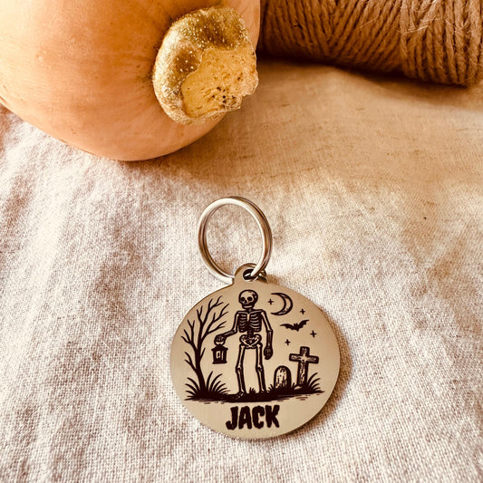 Stainless steel pendant with skeleton design and 'Jack' text on a textured fabric background.