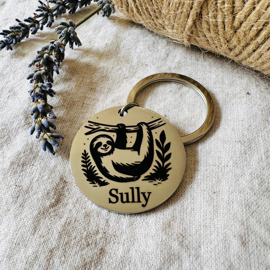Pet id tag with sloth design and 'Sully' engraving on a textured surface with lavender and twine.