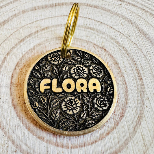 Dog tag with a floral pattern 'Flora' text on a black background. 