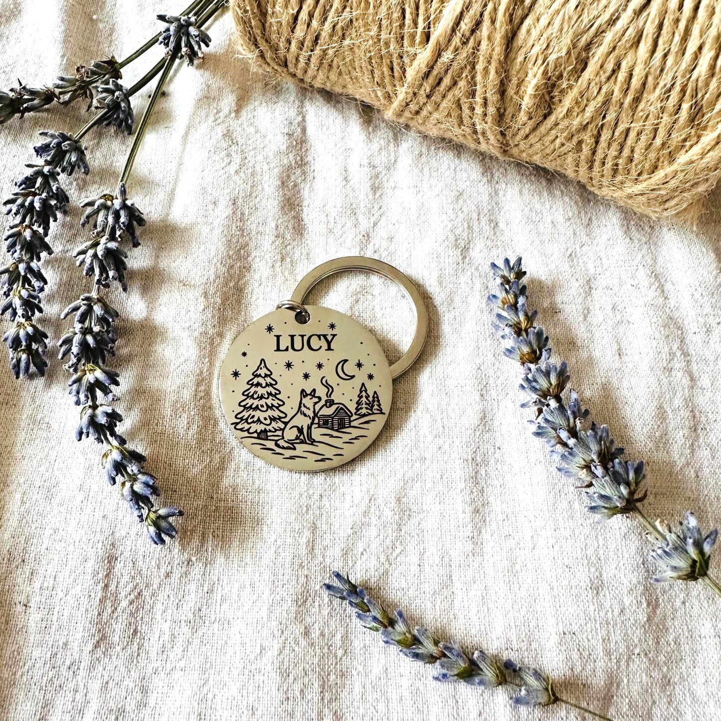 Dog tag with 'Lucy' engraving on a textured surface with lavender and yarn.